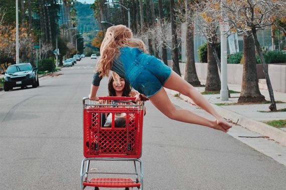 Image of two girls laughing while pushing a shopping cart down a street