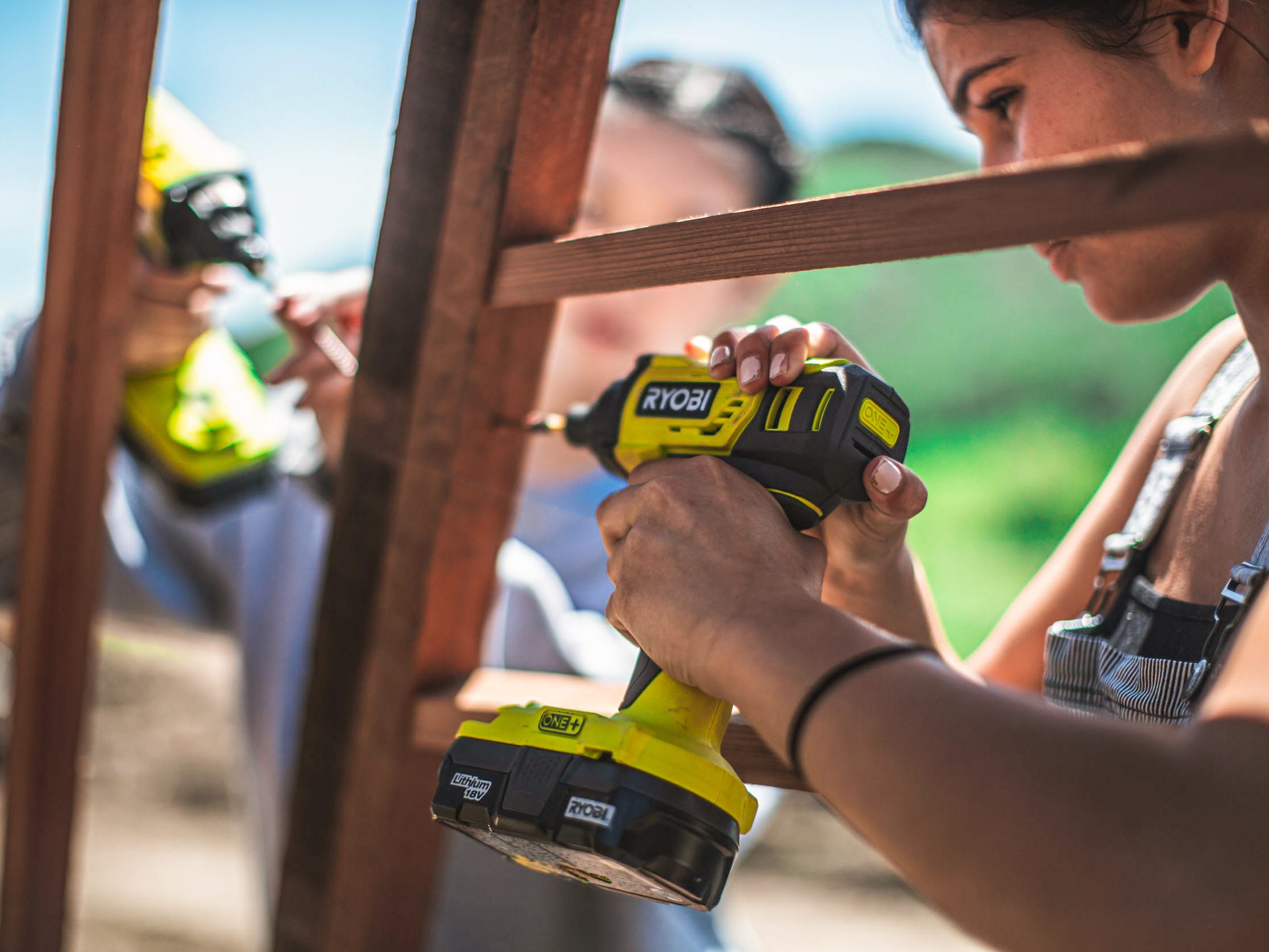 closeup through the wooden frame of two young women using drills to assemble the dome