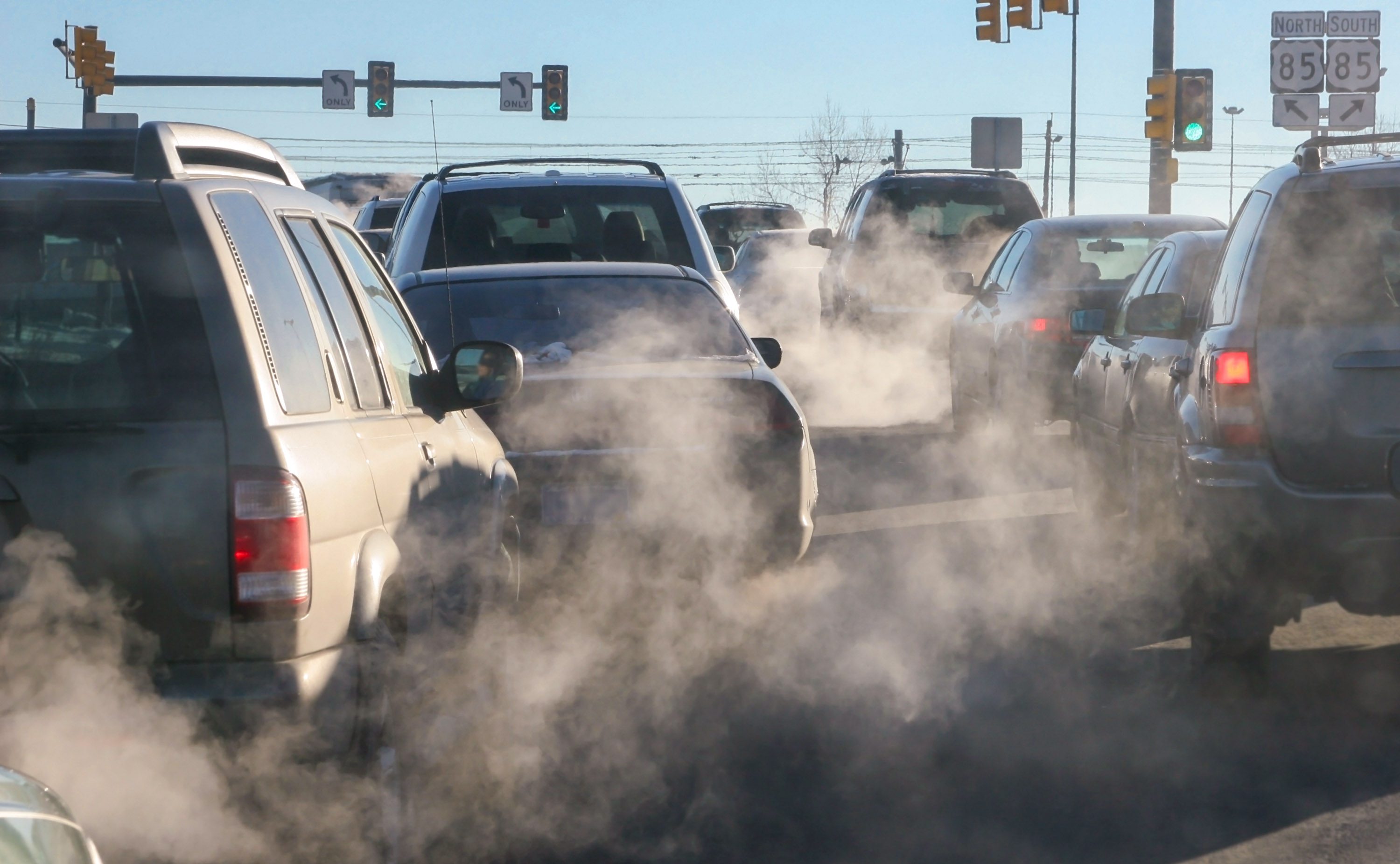 At an intersection, exhaust pours out of the tailpipes of vehicles.
