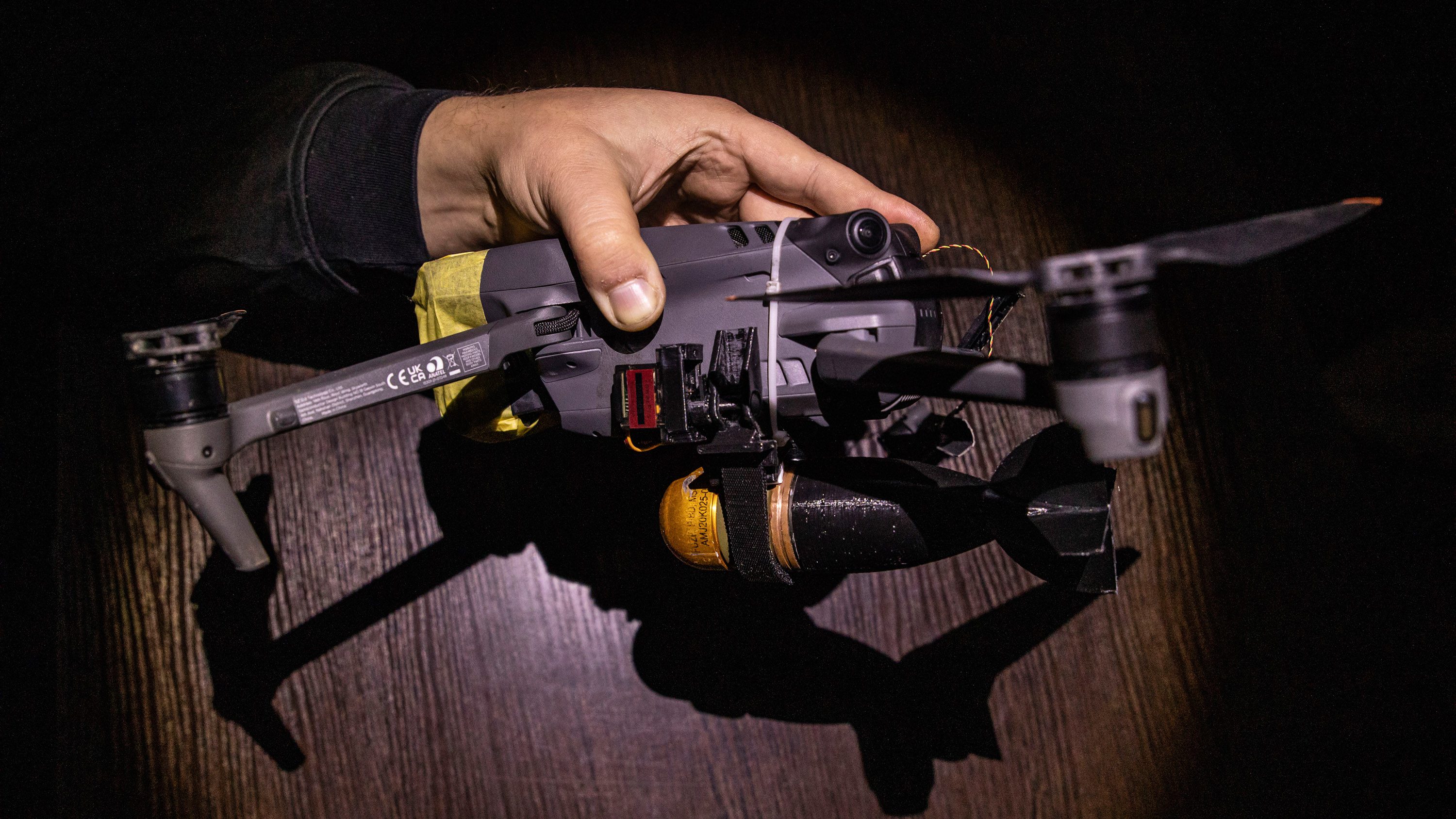 Hand holds a small quadcopter drone with a bomblet attached.