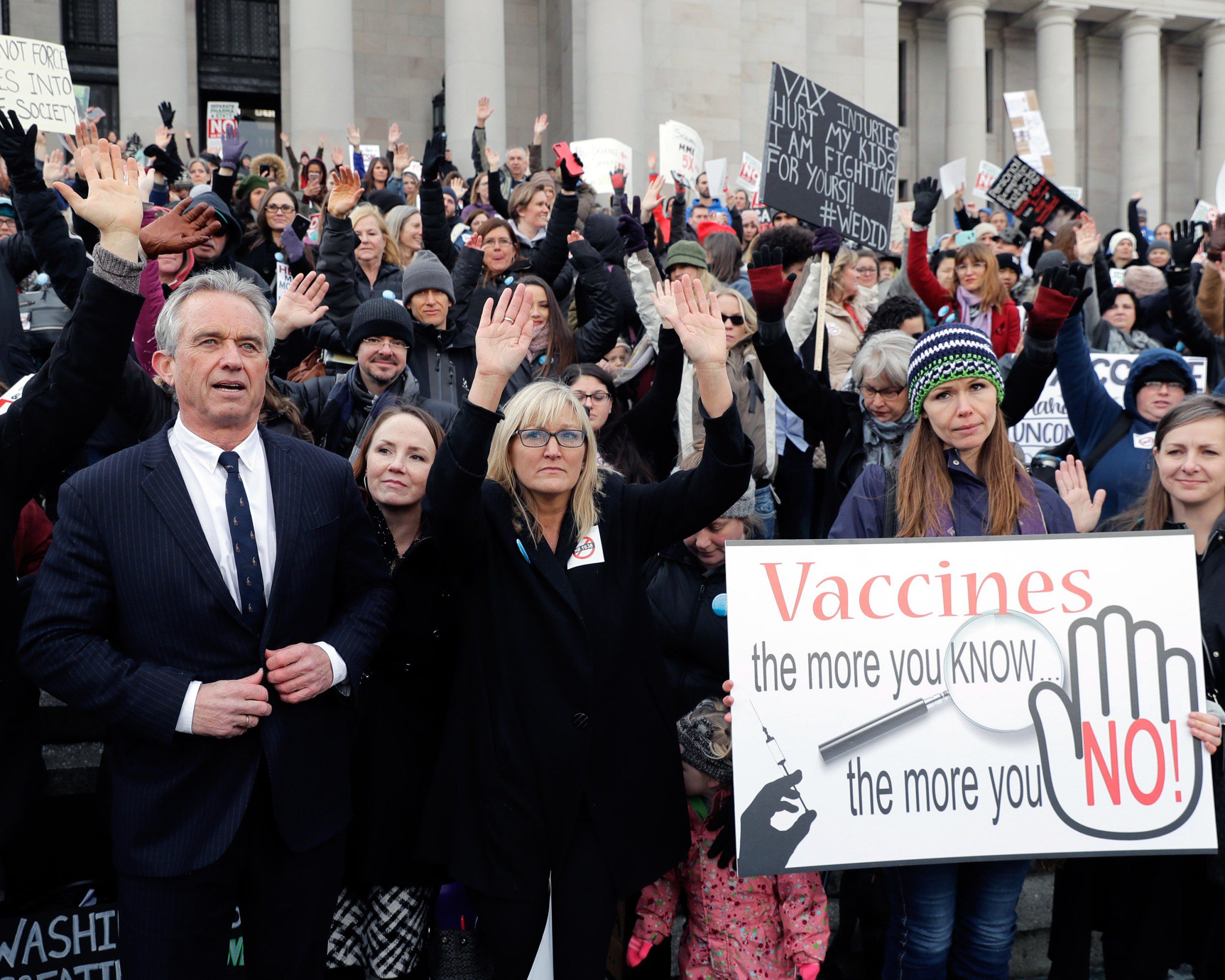 Robert Kennedy Jr. at the Washington state capitol among a group of anti-vax protestors. Sign in the foreground reads, 