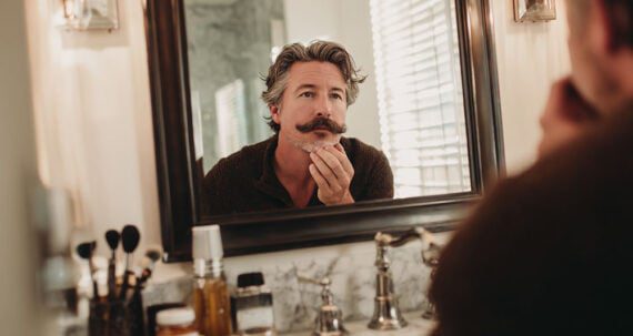 Man with a mustache looking in a mirror