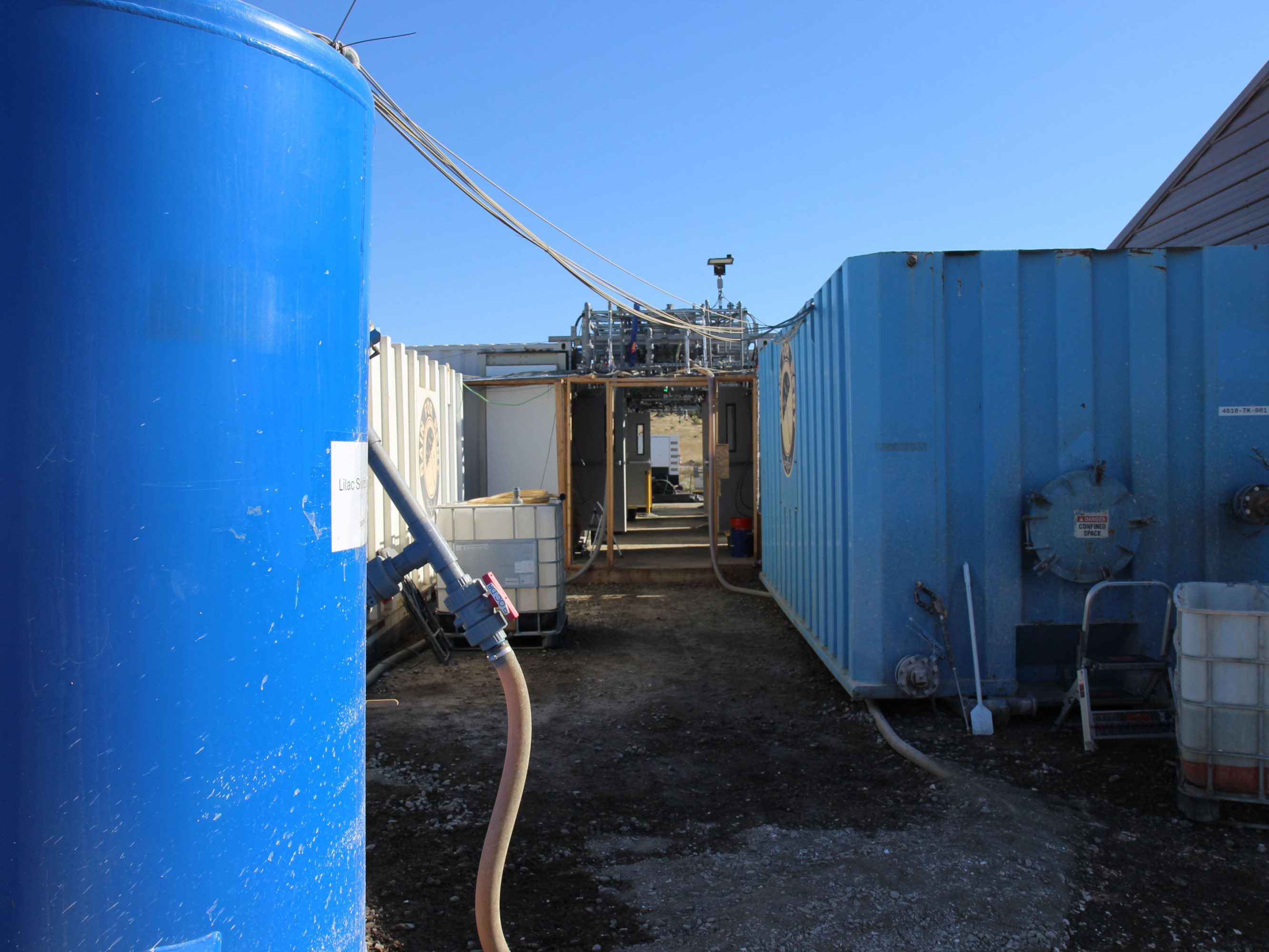 walking path between several tall blue tanks connected by hose