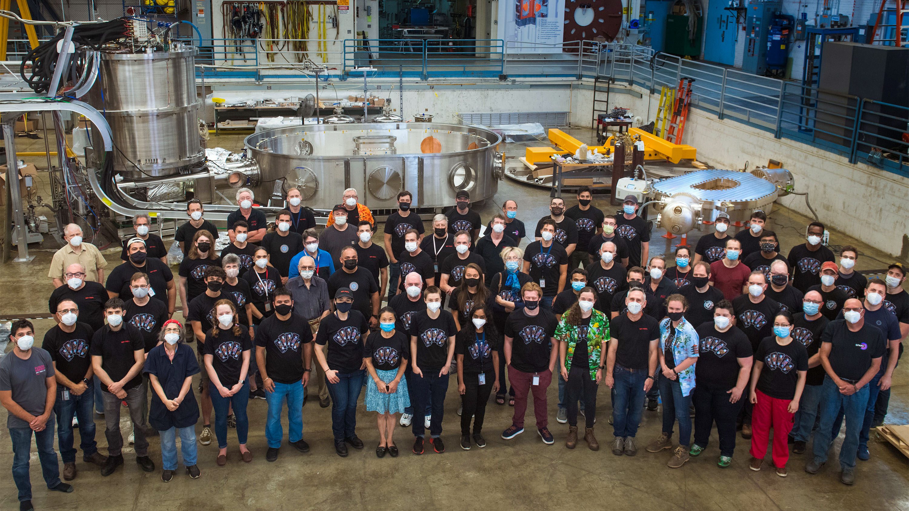 group photo of team standing in the warehouse in front of the reactor