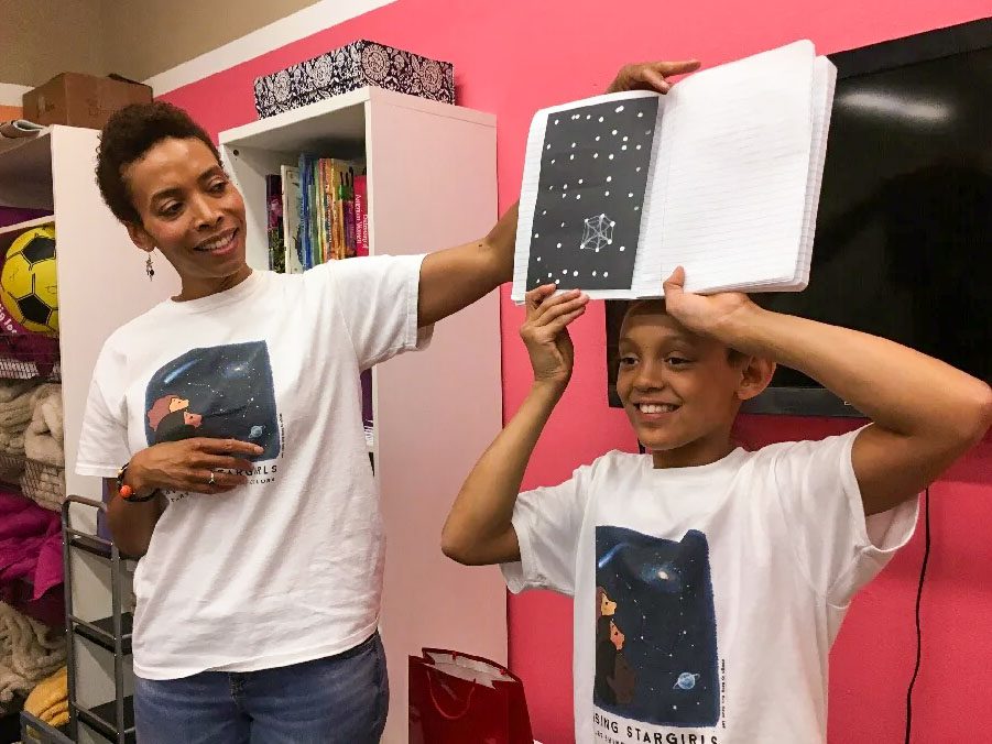 Shields stands next to a child who is holding an open notebook above their head