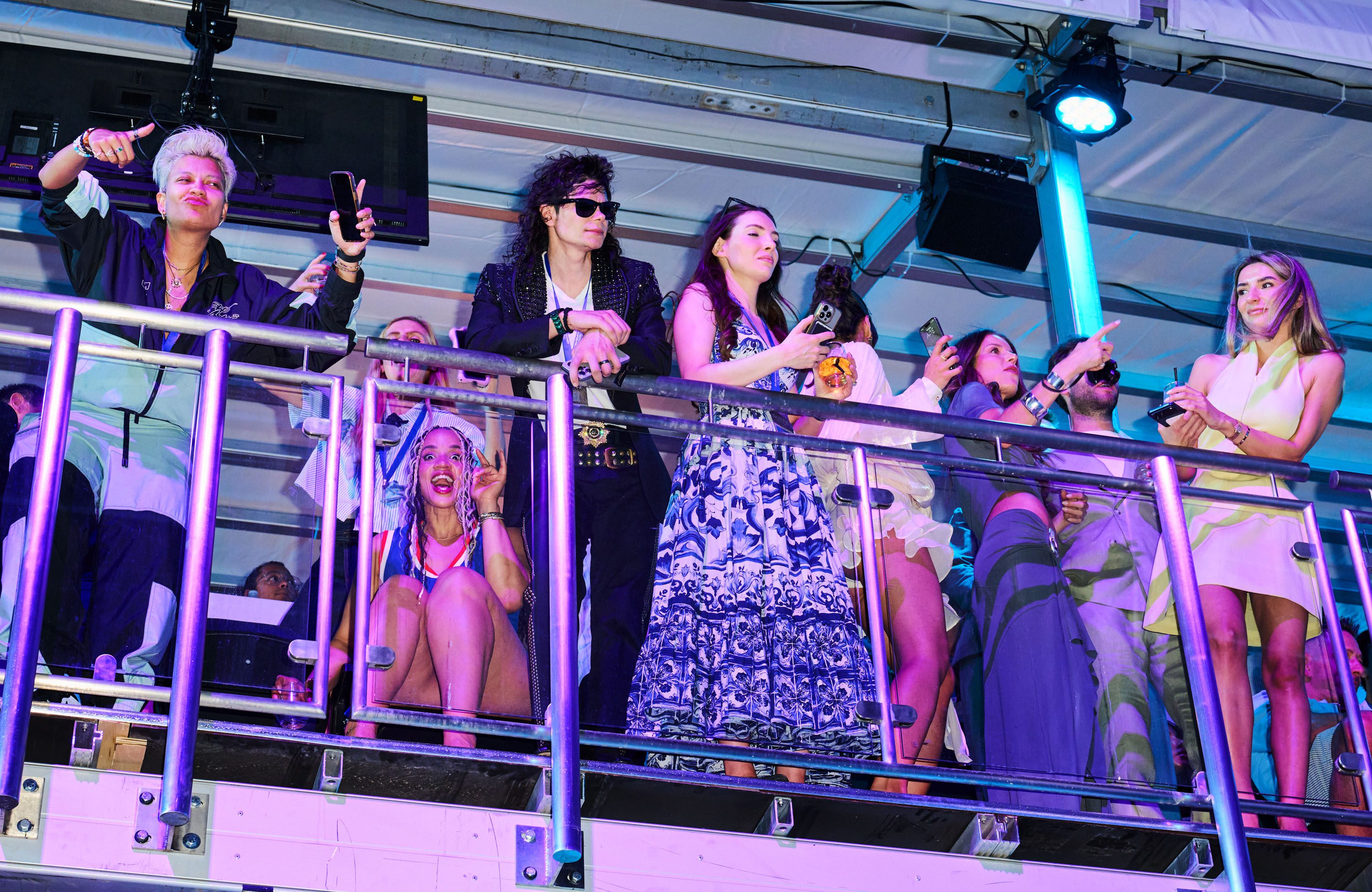 looking up at a balcony of excited attendees including a person at center who is dressed to resemble Michael Jackson.